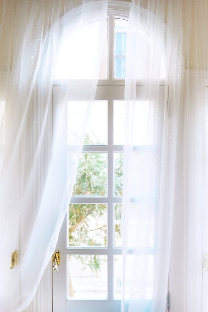 Spacious light house with white entrance door with windows and golden handle located under transparent curtains in daylight